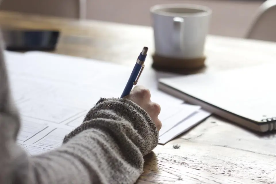 Persona esbozando sobre papel la estructura de una web, junto a una taza de café