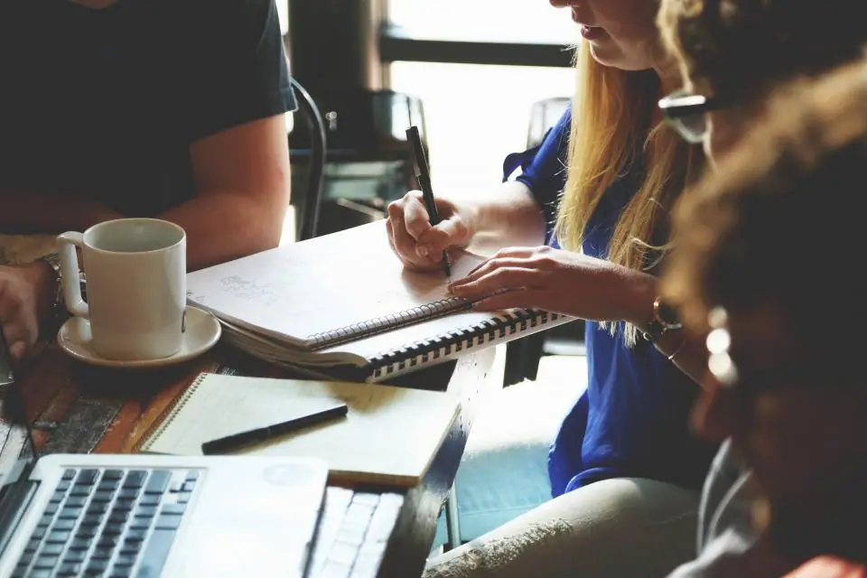 Sesión de trabajo en equipo alrededor de una mesa con cuadernos y un portátil